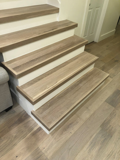 Overhead view of modern light-hardwood stair treads with white risers matching the wood floor